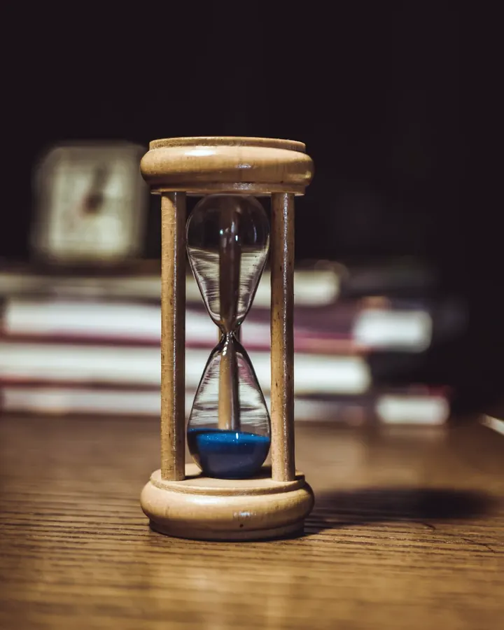 Wooden hourglass with blue sand on a desk